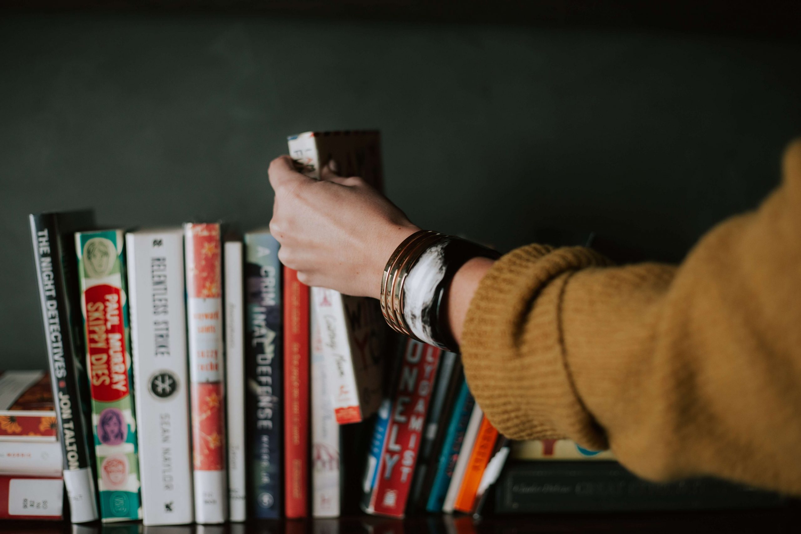 a woman's hand selecting a book off of a shelf.