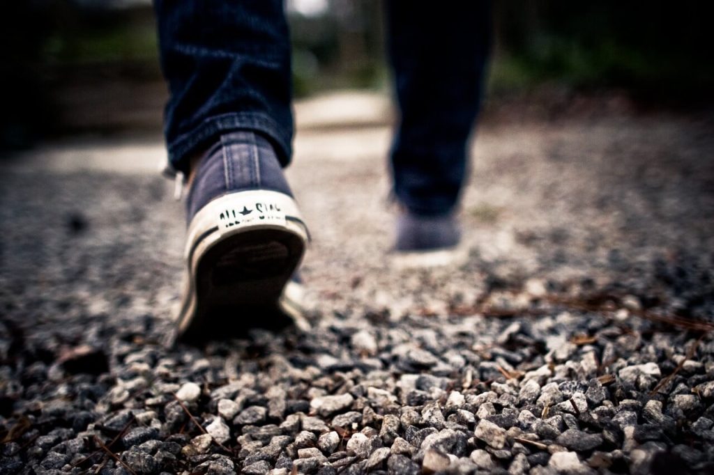 A close up of someone's blue Converse sneakers walking on gravel.